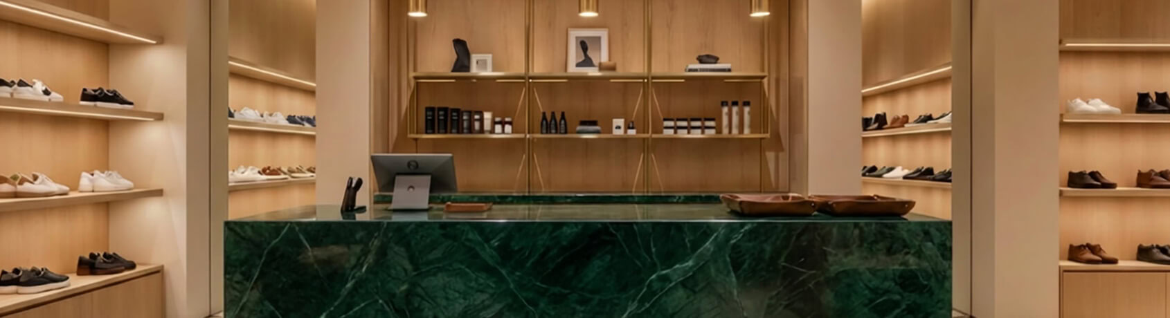 Showroom alanında yeşil mermer banko, aydınlatmalı vitrin rafları ve pirinç sarkıt aydınlatma detayları ile modern mağaza ve showroom uygulaması